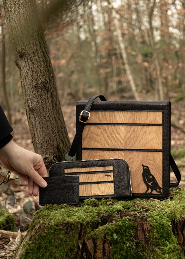 Ein Set aus schwarzen Lederwaren mit eingearbeiteten naturfarbenden Holzelementen. Quadratische Tasche, Gelbbörse. und Gürtel